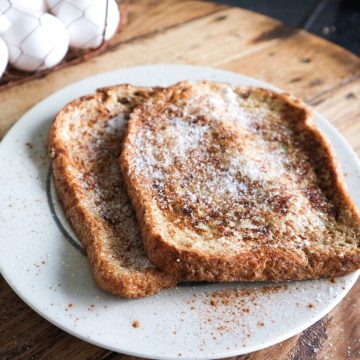 Twee wentelteefjes op een wit bord bestrooit met suiker en kaneel.