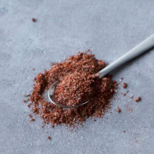 Hamburger kruiden op een lepel met een grijze achtergrond.