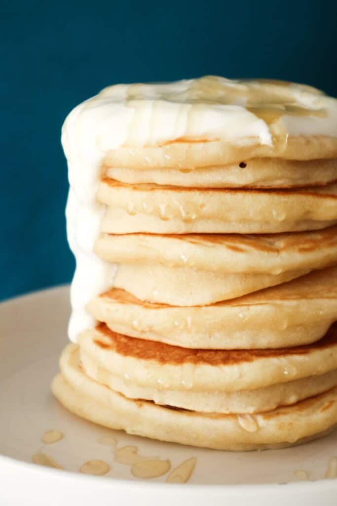 een stapel pannenkoeken gemaakt met havermelk op een wit bord met yoghurt en honing