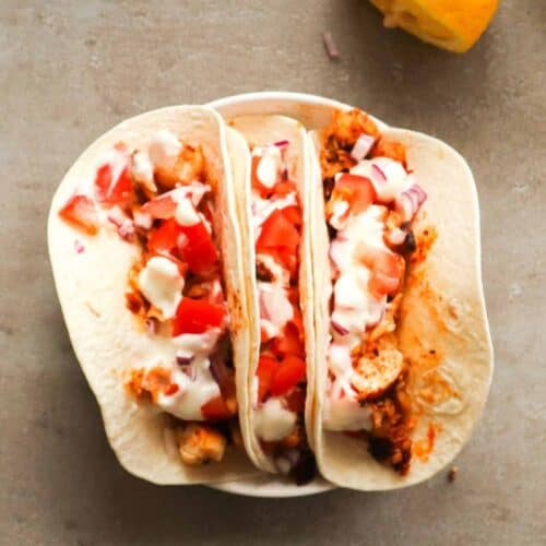 Een overhead shot van drie taco's met vis, tomaat en zelfgemaakte yoghurtsaus