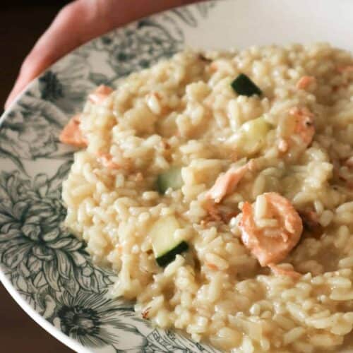 een close up van risotto met zalm op een wit bord met groene opdruk
